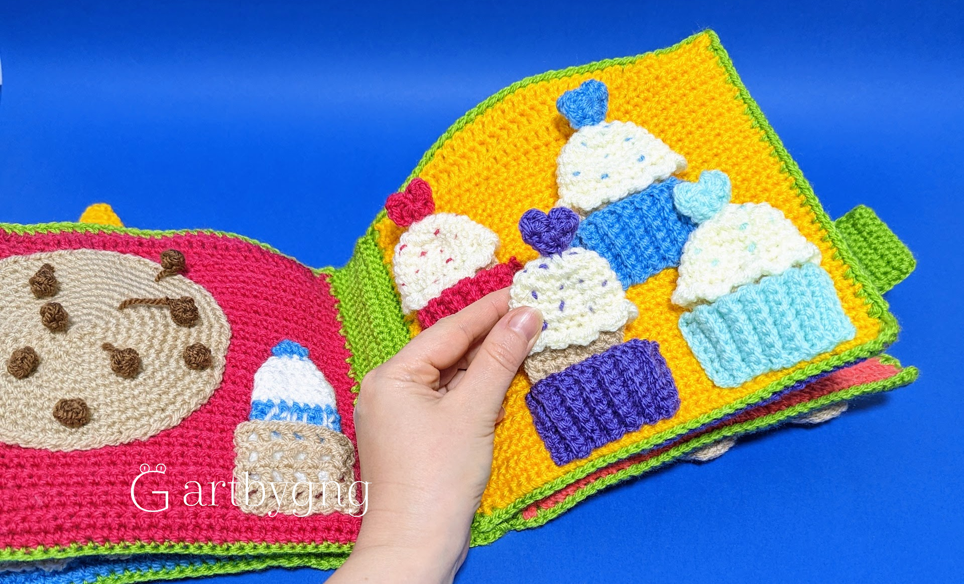 A hand placing a crocheted cupcake onto its matching color liner, with a cookie page and milk carton on the facing page
